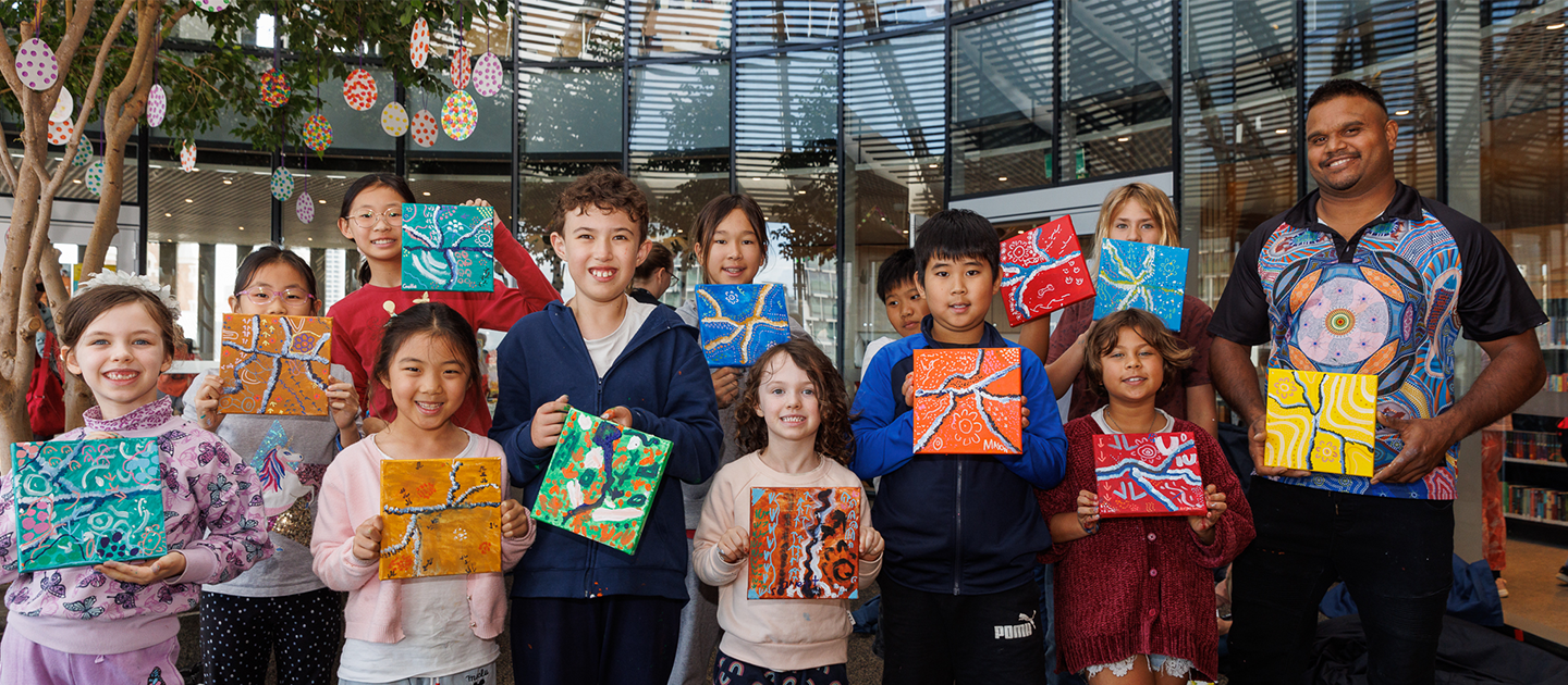 Justin Martin and children holding up artwork from an art workshop. 