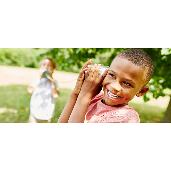 Two children playing with a tin-can telephone outside in a park.