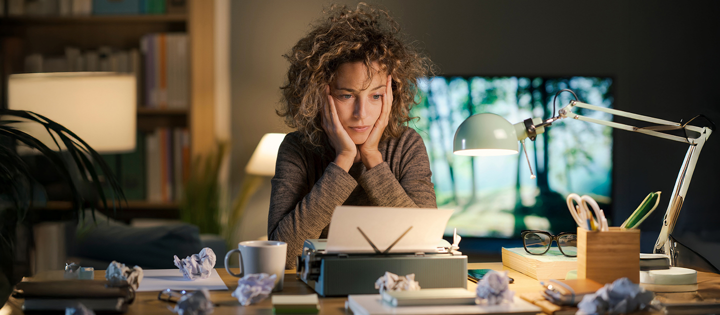 Woman sat at desk with face in hands, staring at her writing draft.