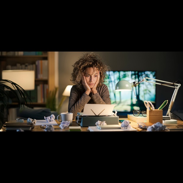 Woman sat at desk with face in hands, staring at her writing draft.