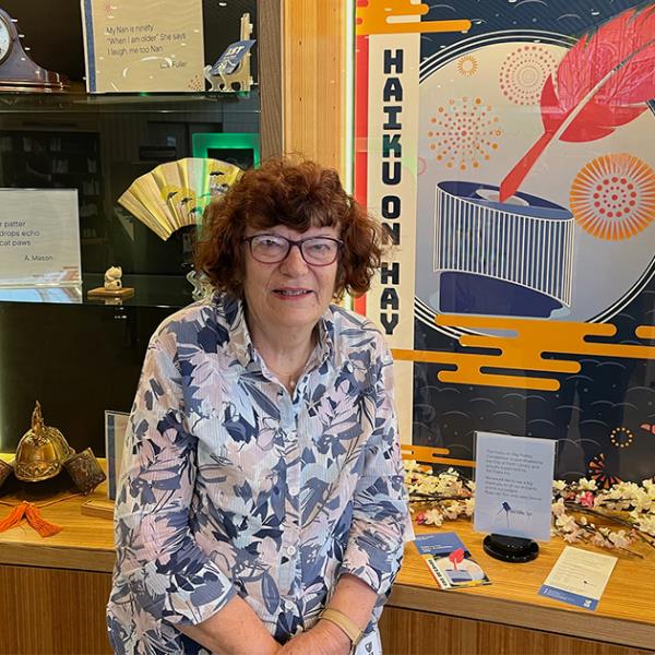Photo of poet and writer Rose van Son sitting in front of the Haiku on Hay display at the Library.