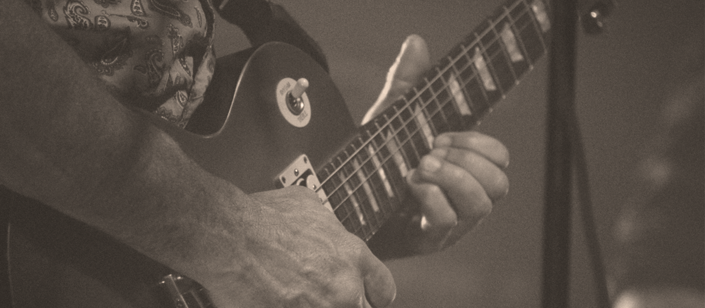 Close up sepia photograph of a man playing an electric guitar on stage. 