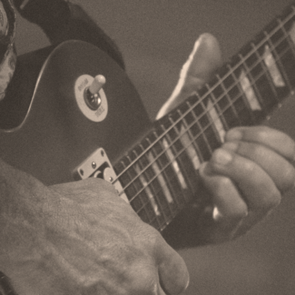 Close up sepia photograph of a man playing an electric guitar on stage.