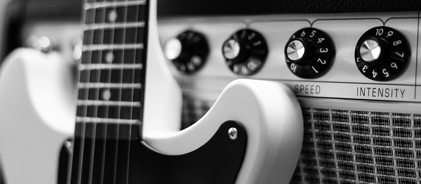 Close up black and white photograph of an electric guitar leaning against a retro amplifier. 