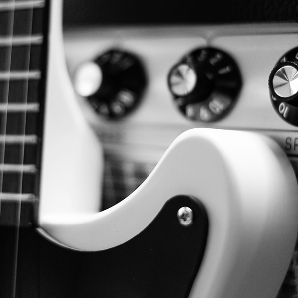 Close up black and white photograph of an electric guitar leaning against a retro amplifier.