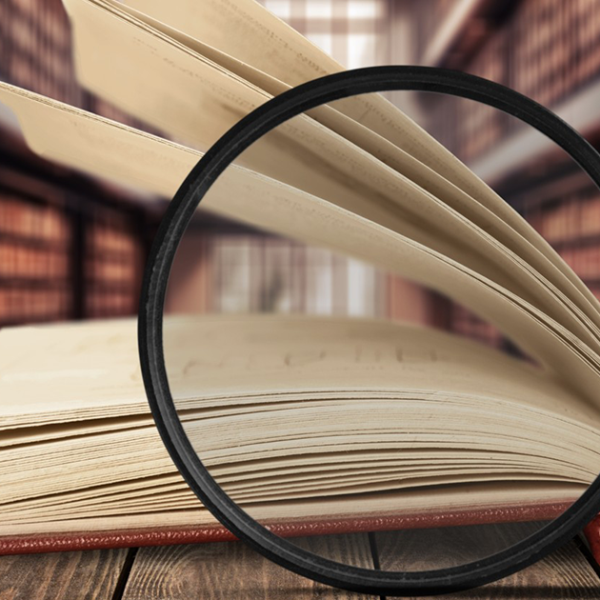 Magnifying glass in front of a book, with a library background.