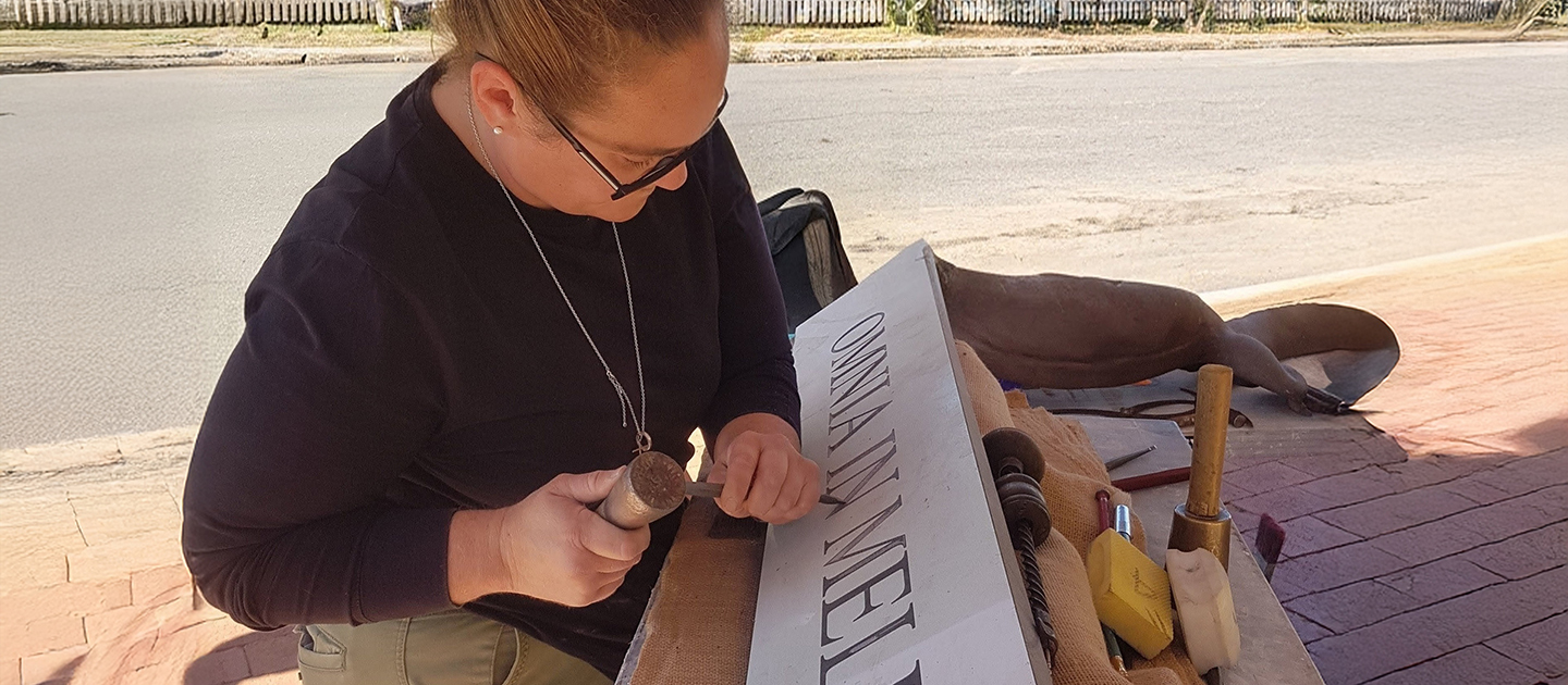 Lady stonemason working outside on a stone feature with Latin inscription.  