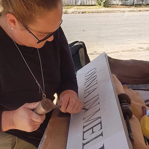 Lady stonemason working outside on a stone feature with Latin inscription.