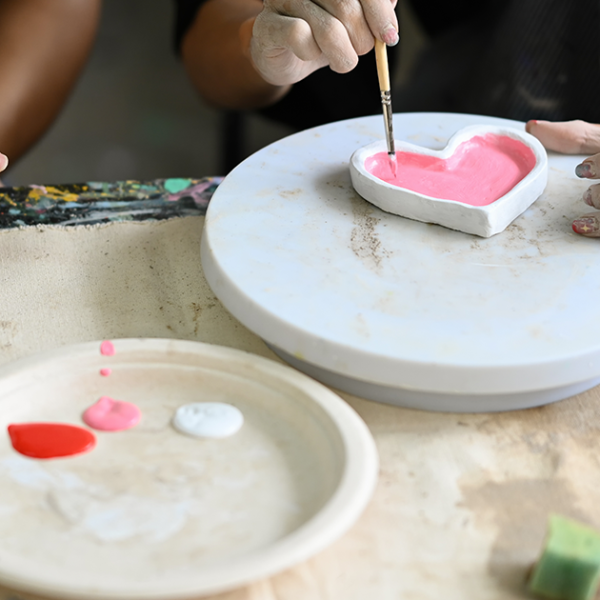 View of a worktable with two young people decorating an air clay heart-shaped dish.