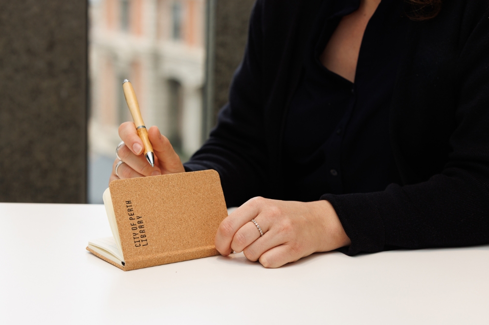 A person using a City of Perth Library branded pen and notebook