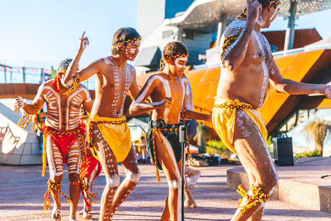 Aboriginal children and adults dance wearing coloured outfits